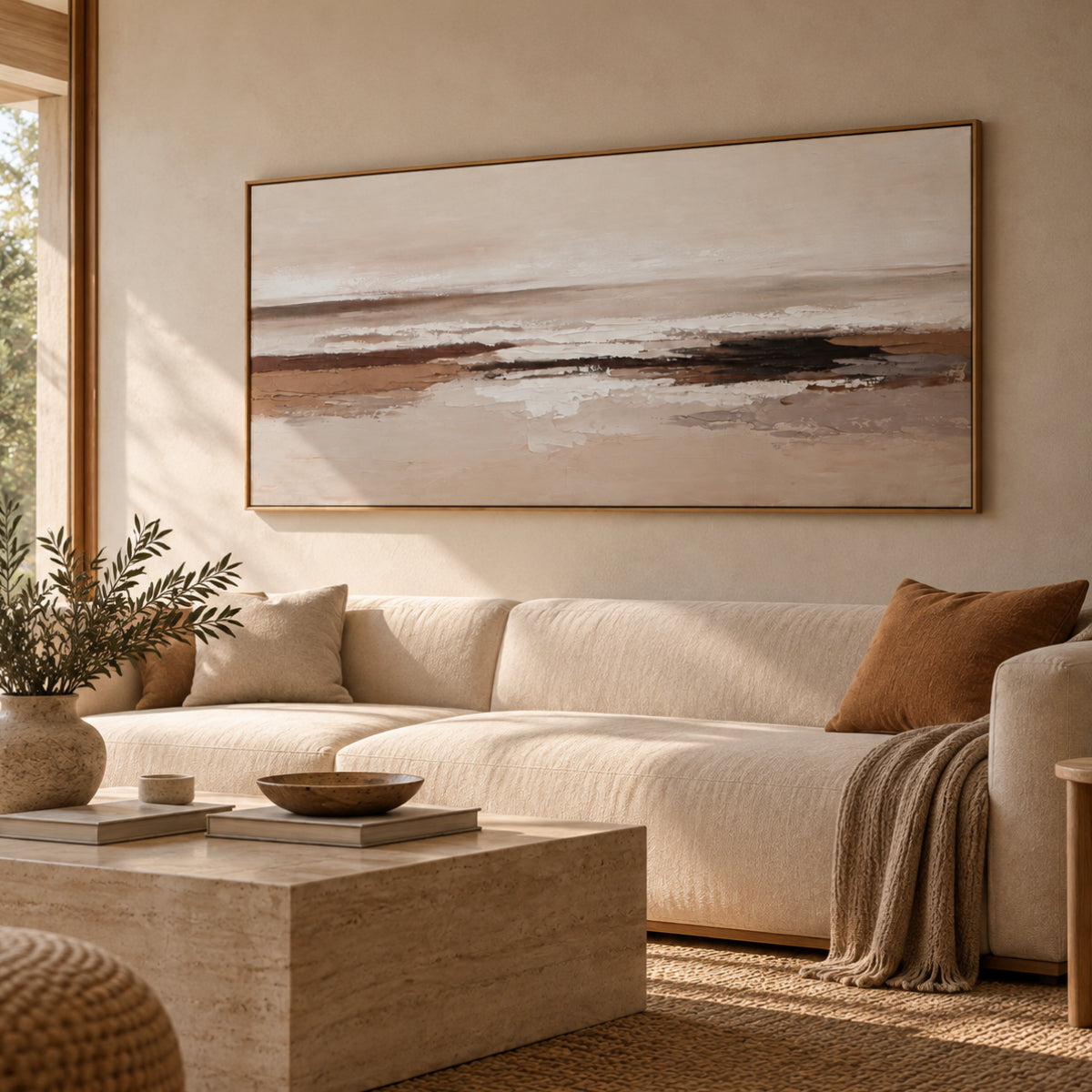 Cuadro abstracto horizontal en tonos beige, marrón y blanco con detalles texturizados y marco de madera, decorando un salón de estilo mediterráneo sobre un sofá claro.