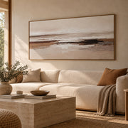 Cuadro abstracto horizontal en tonos beige, marrón y blanco con detalles texturizados y marco de madera, decorando un salón de estilo mediterráneo sobre un sofá claro.