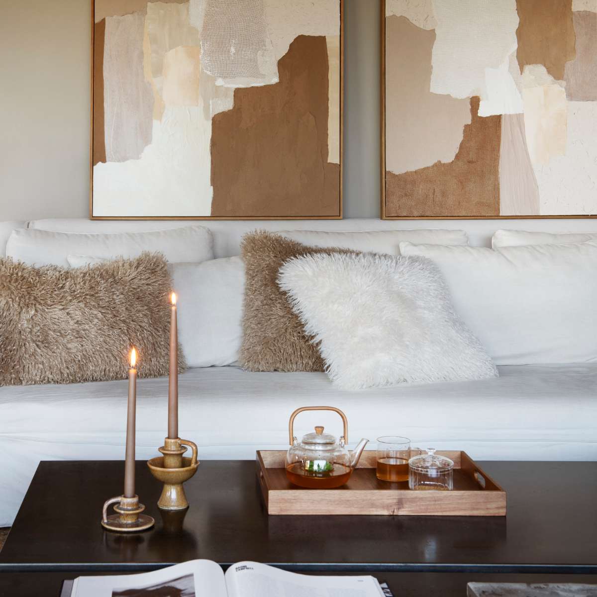 Salón elegante con sofá, cojines y cuadros  en tonos beige marrón y blancos