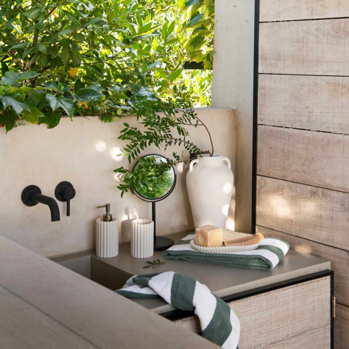 Baño exterior con dispensador de poliresina con rayas beige jarrón decorativo de cerámica y espejo de pie para baño.