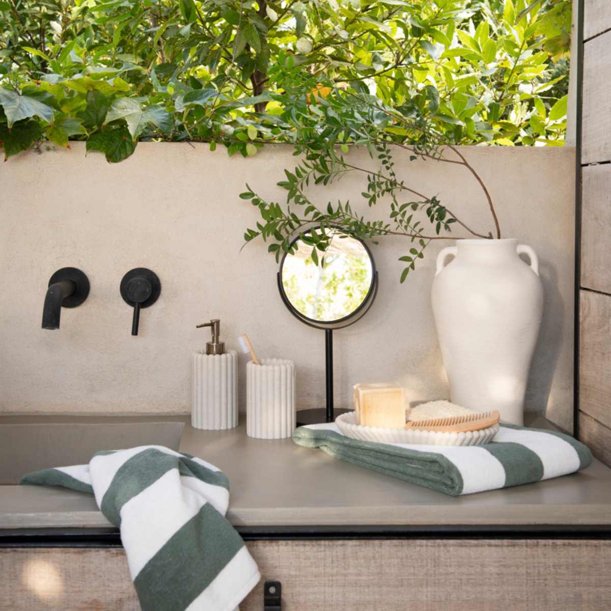 Baño exterior con dispensador de poliresina con rayas beige jarrón decorativo de cerámica y espejo de pie para baño.