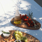 Aceitera de vidrio acanalado con aceite, presentada en una mesa exterior junto a alimentos mediterráneos.