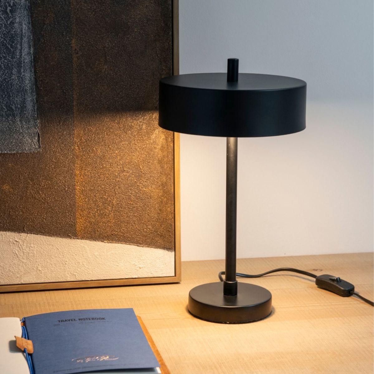 Lámpara de mesa negra encendida sobre escritorio de madera.