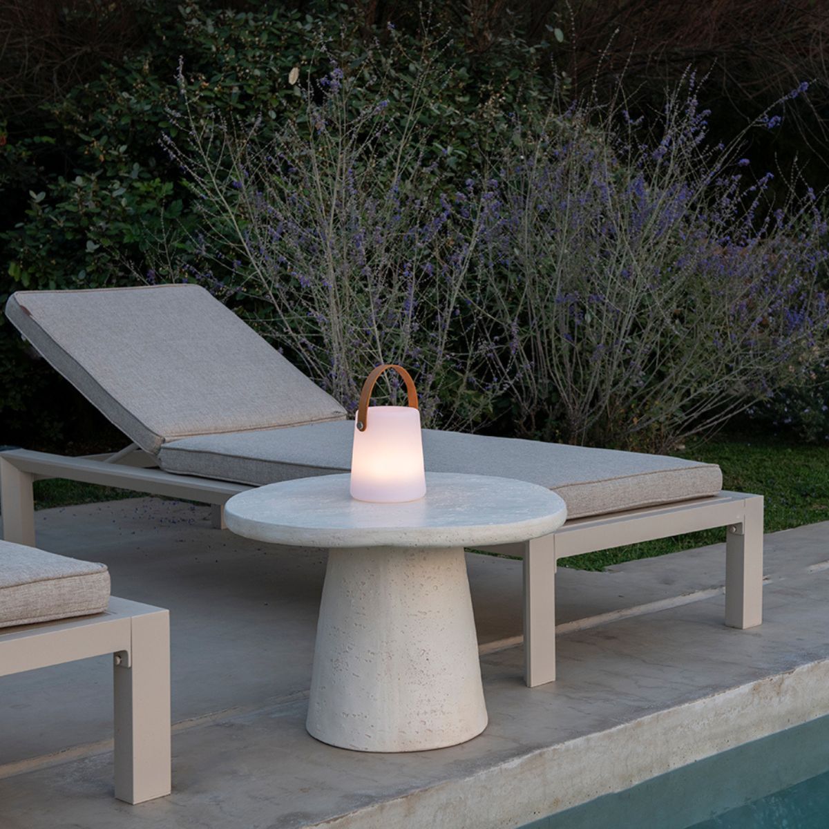 Lámpara LED inalámbrica con remoto sobre mesa de exterior  en jardín con tumbonas