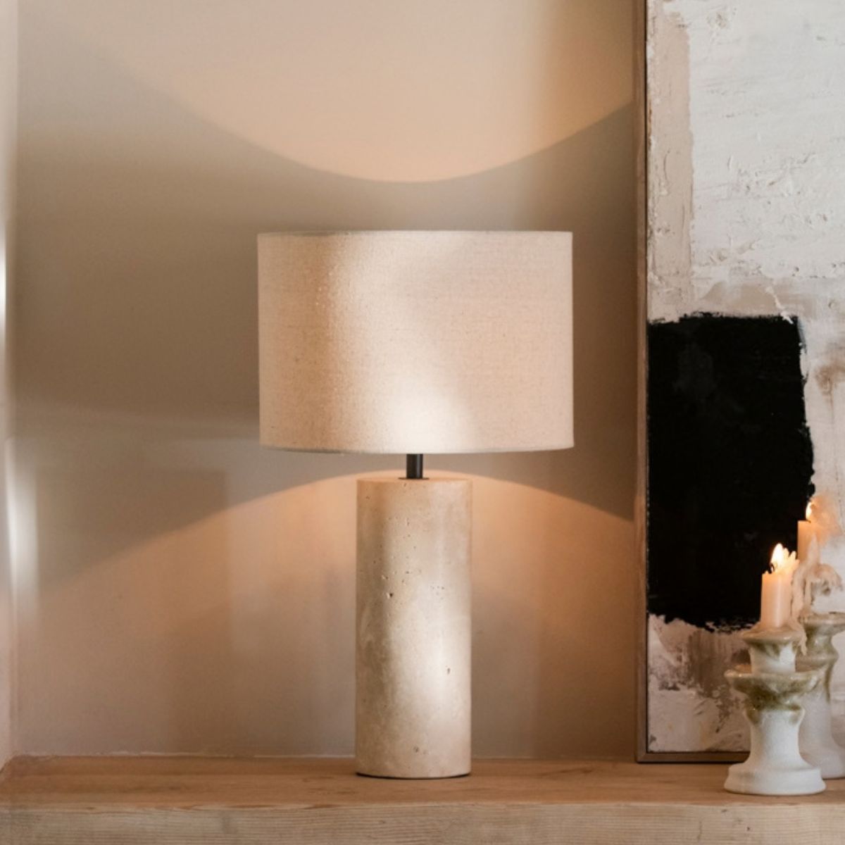 Lámpara de sobremesa encendida con base de piedra beige y pantalla de tela, creando una iluminación ambiental cálida.