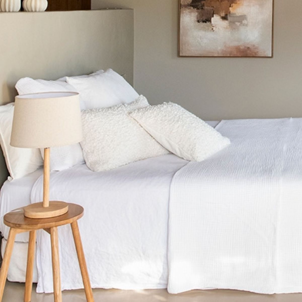 Lámpara de sobremesa de madera con pantalla beige sobre mesita auxiliar junto a la cama.