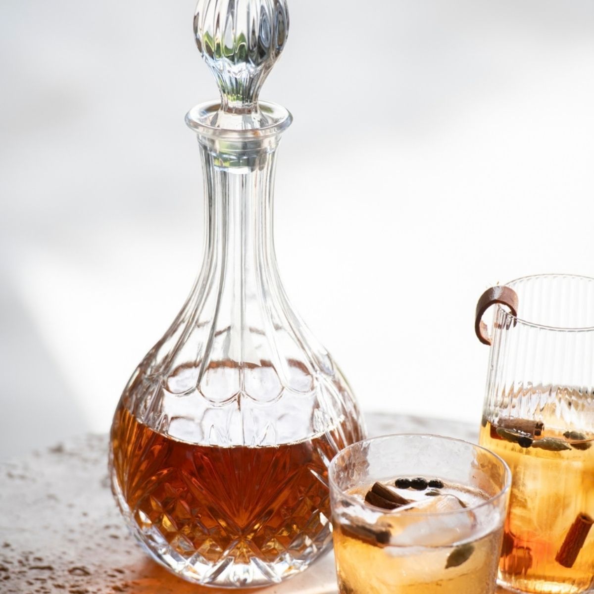 Licorera de vidrio tallado con bebida, acompañada de vasos sobre una mesa.