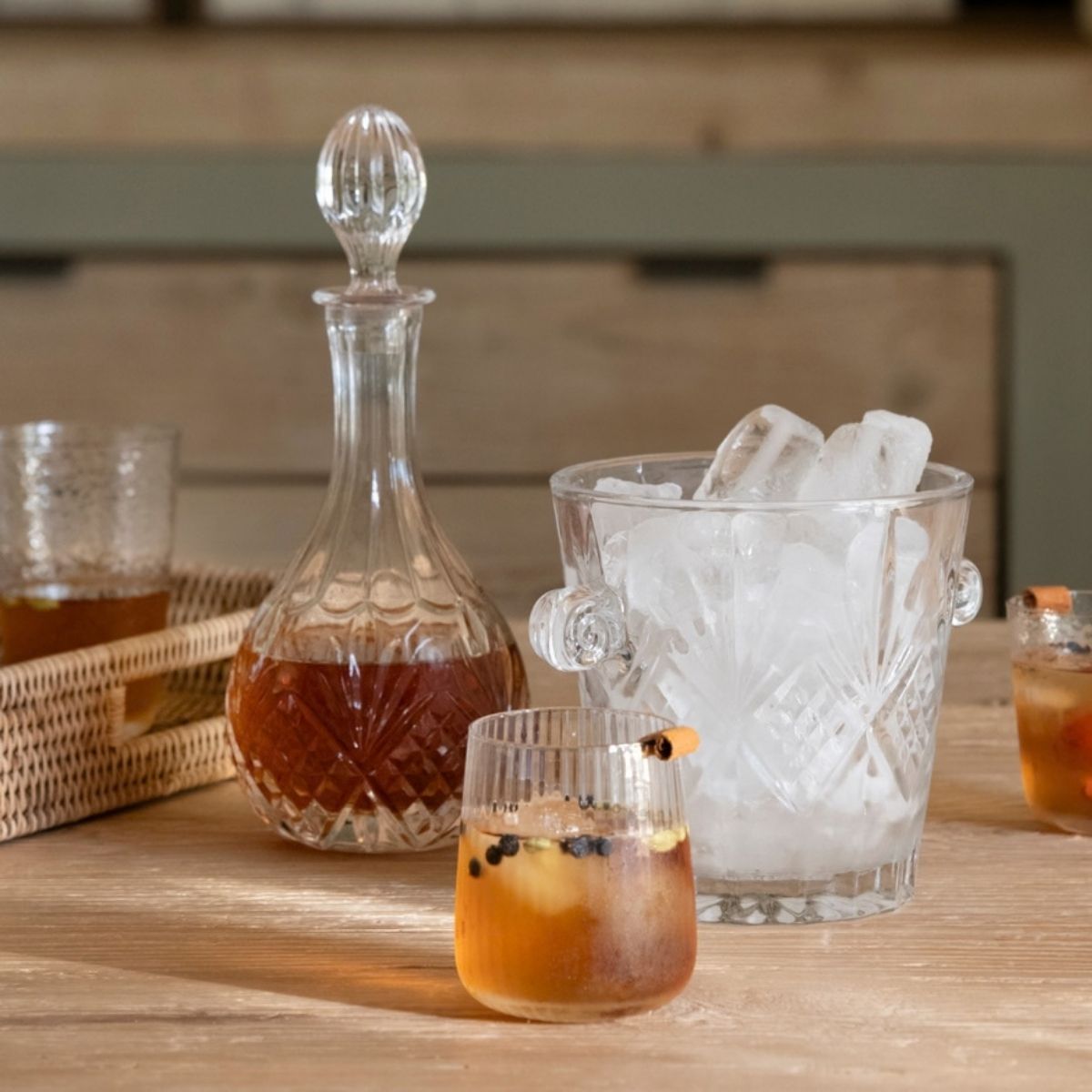 Licorera y cubitera de vidrio tallado con hielo, acompañadas de vasos sobre una mesa.