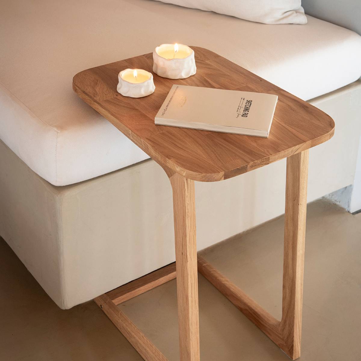 Mesa auxiliar de roble para sofá con diseño funcional y natural colocada junto al sofá.